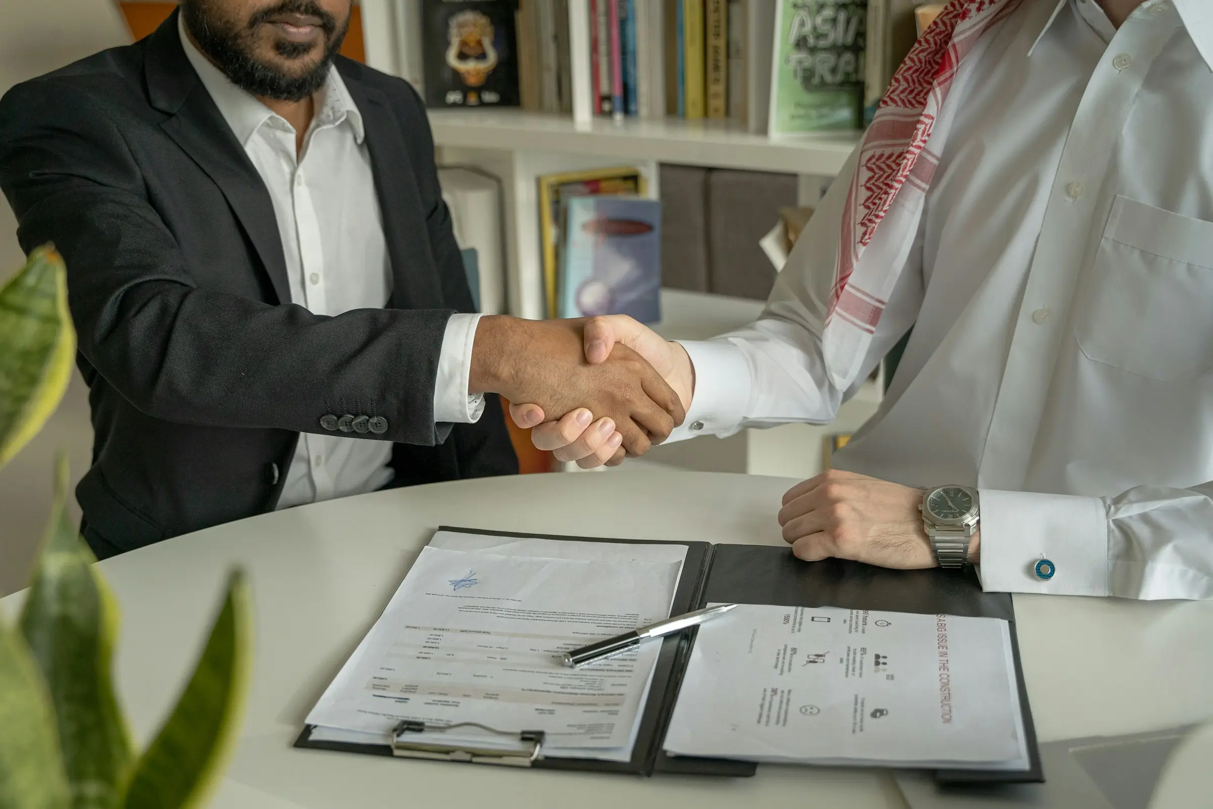 Two men shaking hands across a desk with signed documents
