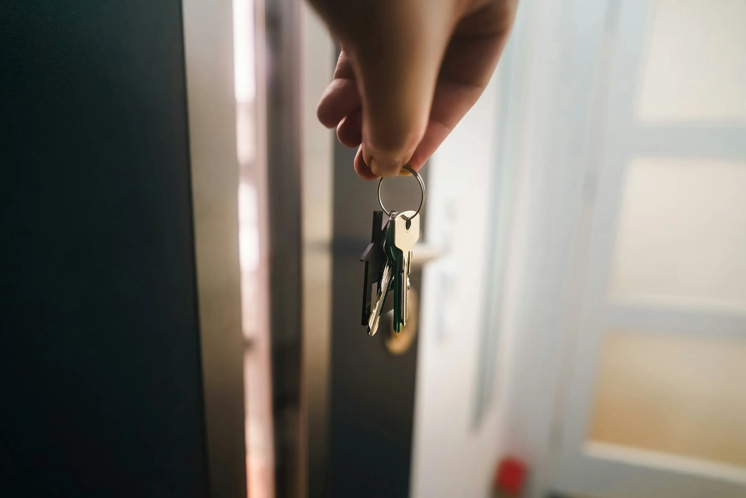 A hand holding a set of house keys at an open front door